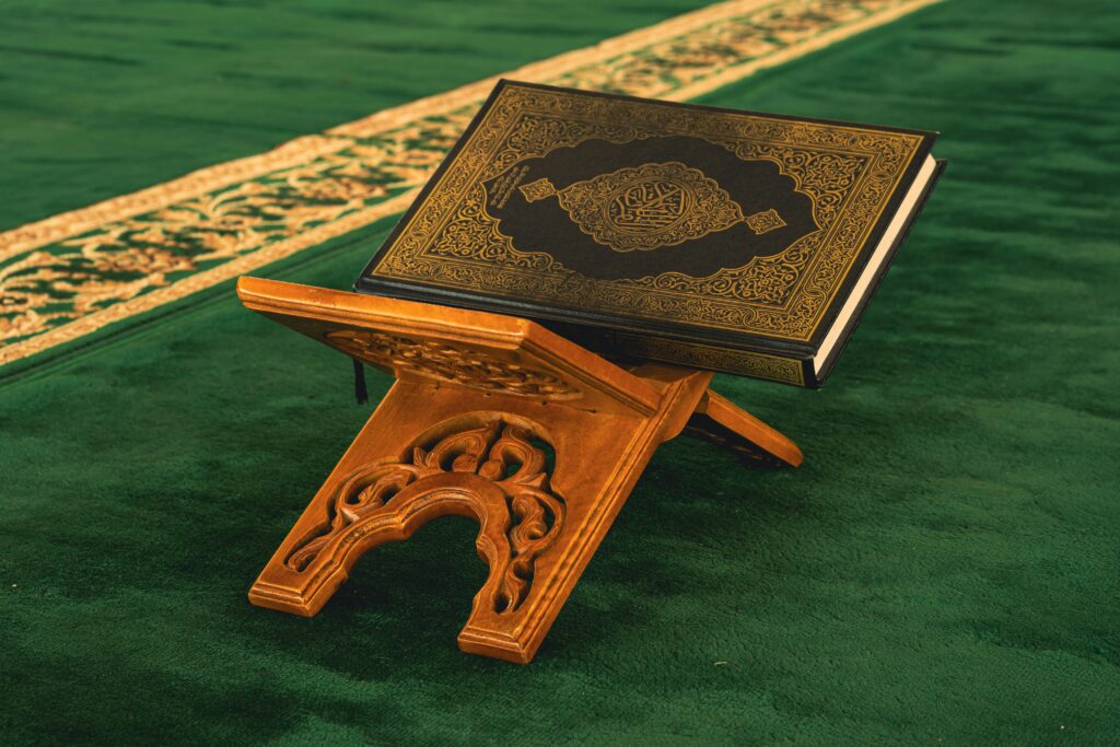 A beautifully ornate Quran placed on a traditional wooden stand in a mosque setting.