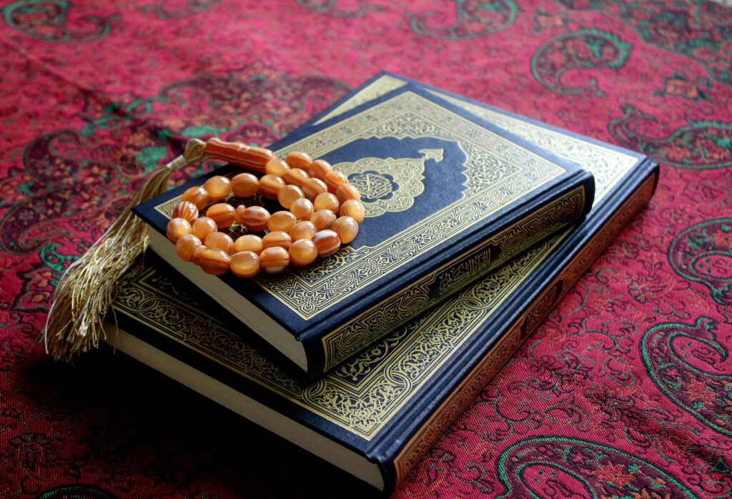An arrangement of the Holy Quran with a Tasbih rosary on a traditional red patterned fabric.