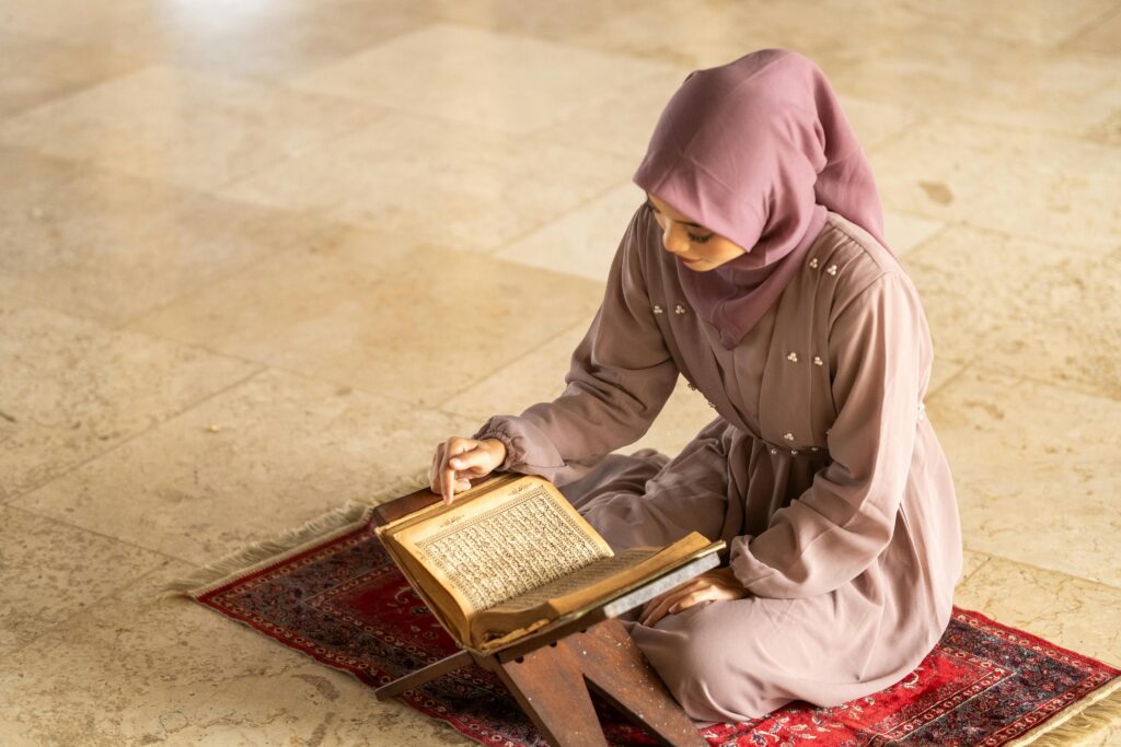 What is the difference between Islam and Muslim? Elegant woman in hijab reading the Quran at a mosque in Jakarta, Indonesia.