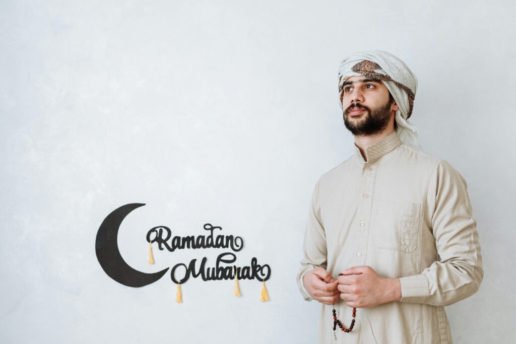 Man in traditional wear celebrating Ramadan with a crescent moon decoration and copy space.